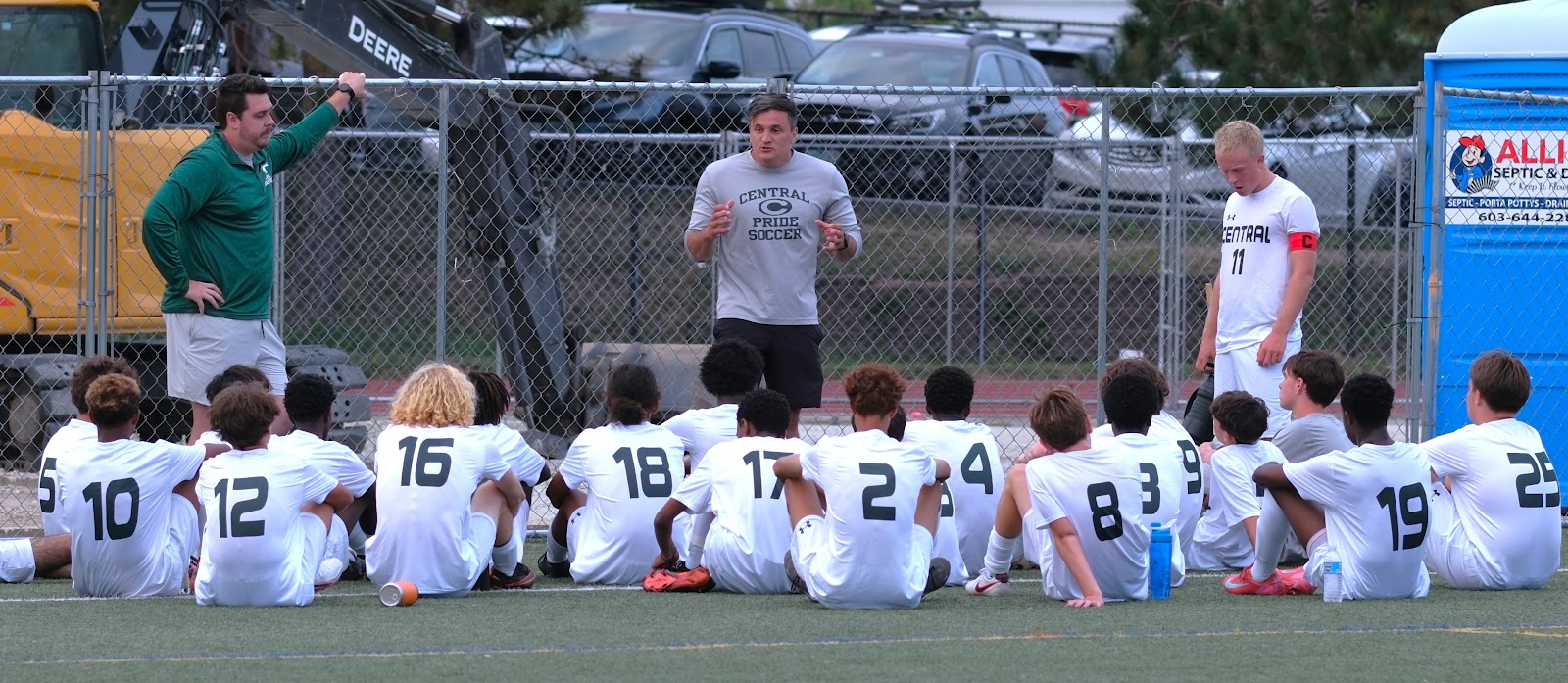 Central head coach speaking to the seated boys' soccer team on the sideline before kickoff